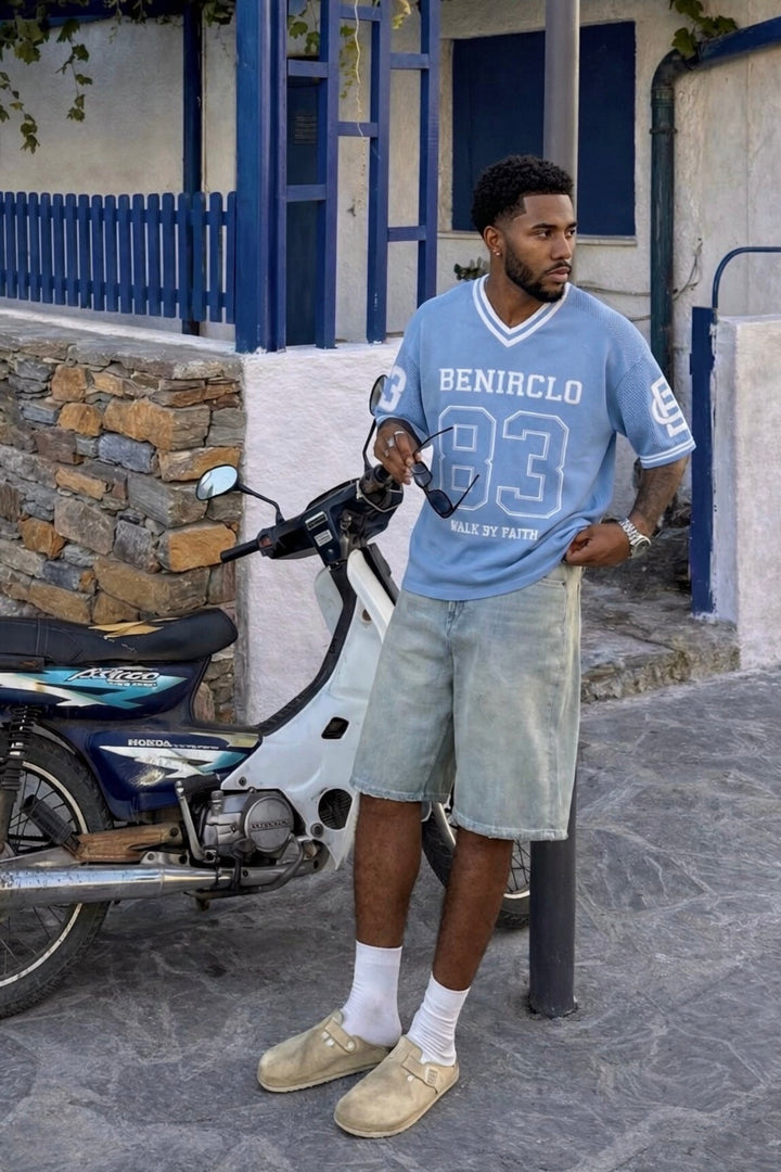 Benir Clothing light blue knit jersey with 83 graphic, worn by a man leaning against a moped outdoors.